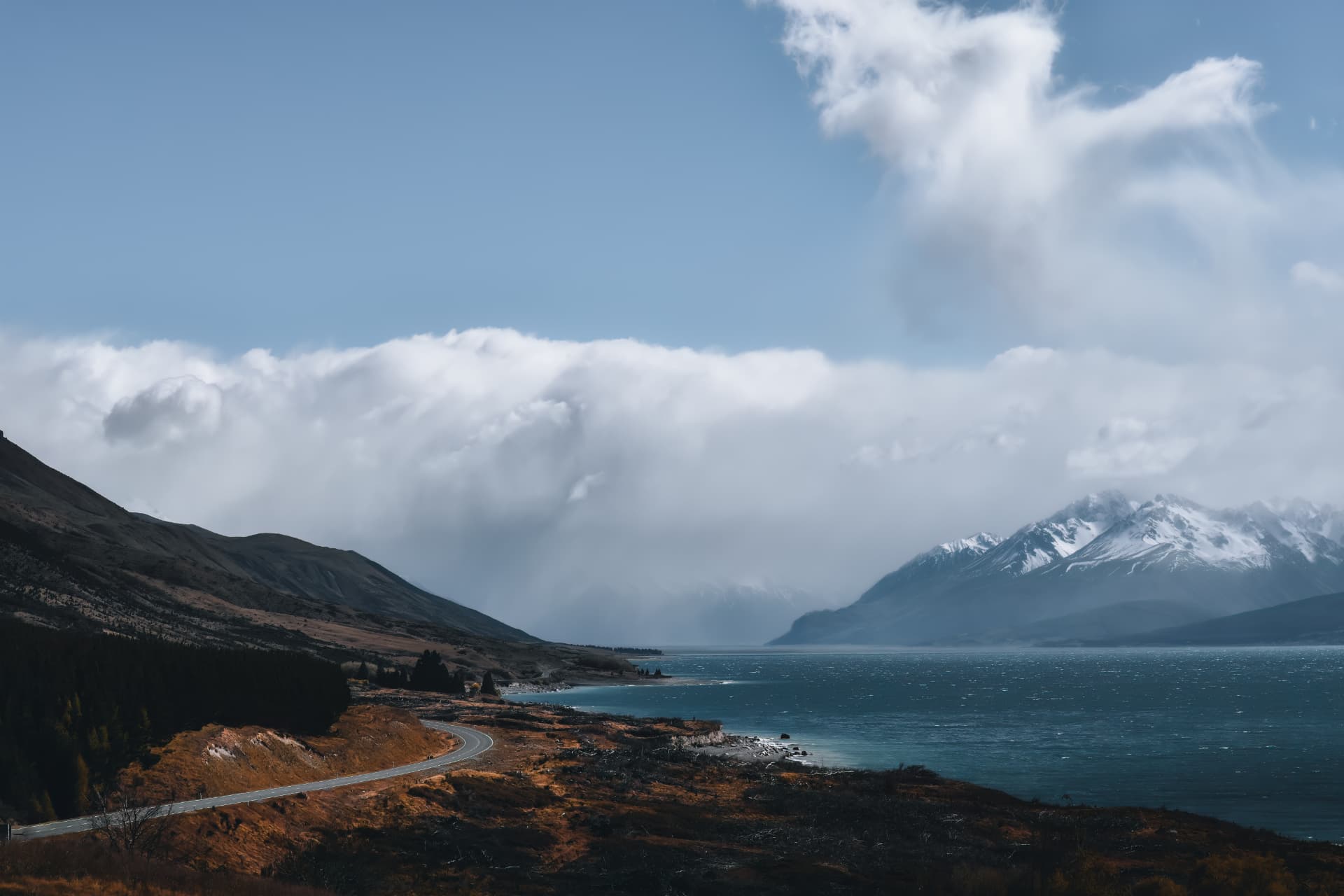 A lake curving beneath snowy mountains and a dark shoreline