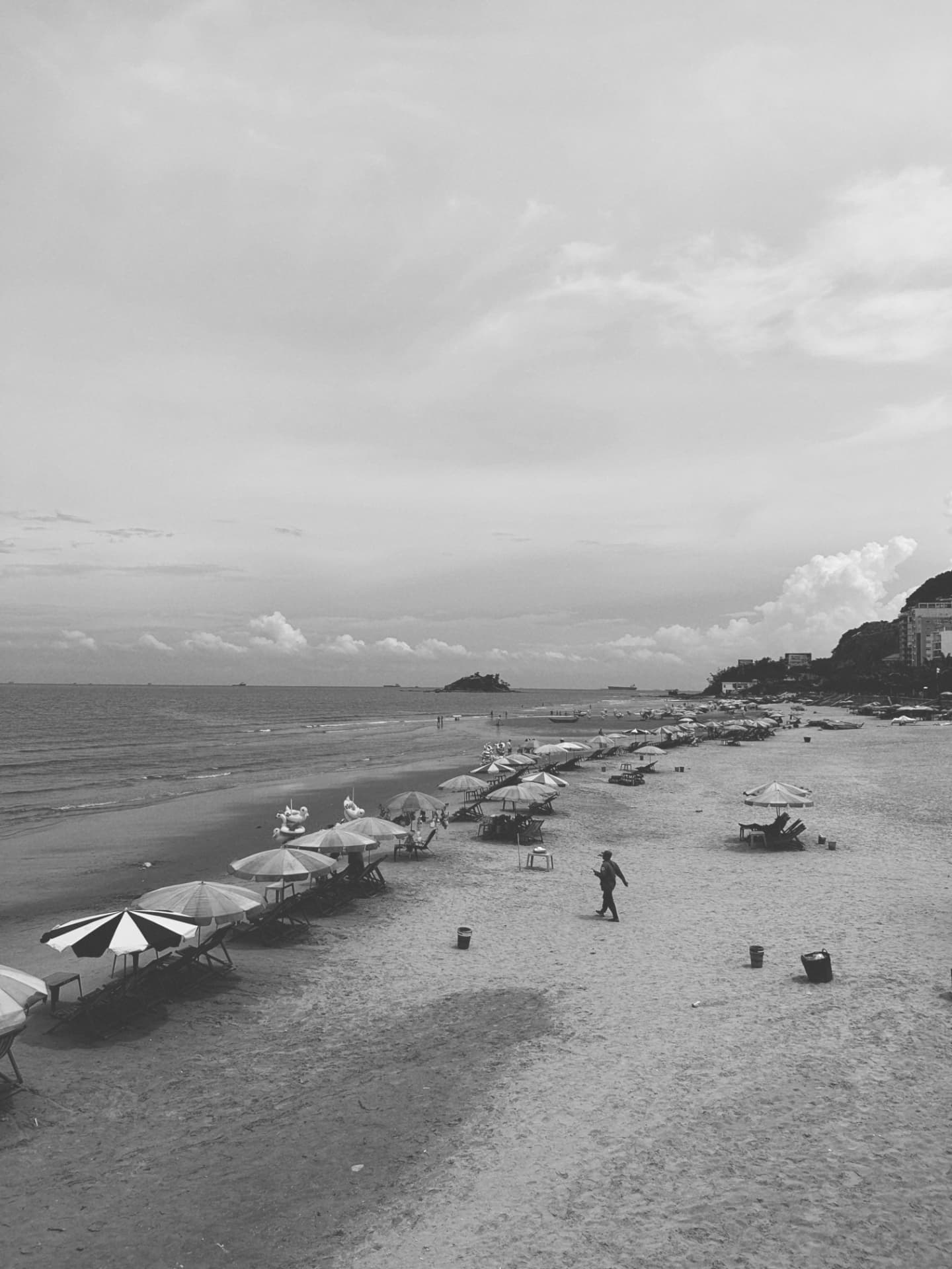 Beach parasols and loungers beneath a lone walker and a distant headland