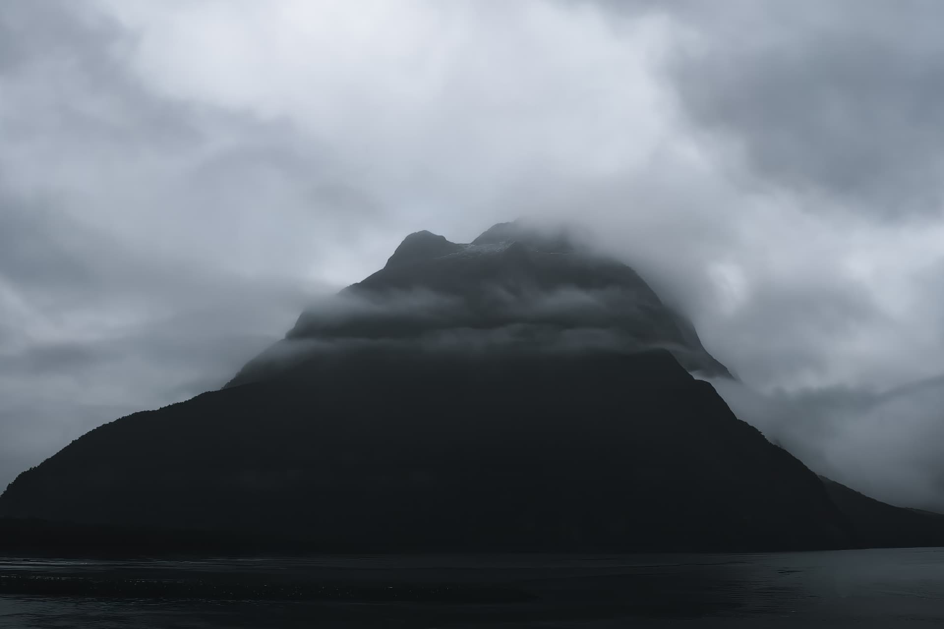 A dark mountain wrapped in cloud above still water