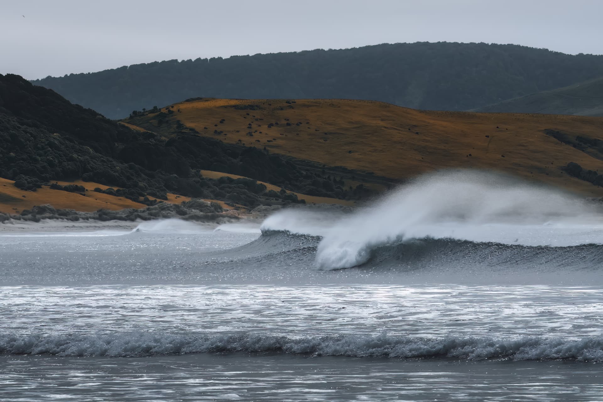 A breaking wave before golden hills