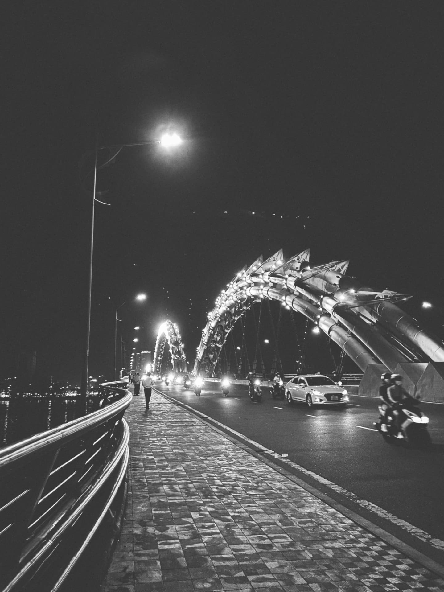 A sculpted bridge arch lit over night traffic on the walkway