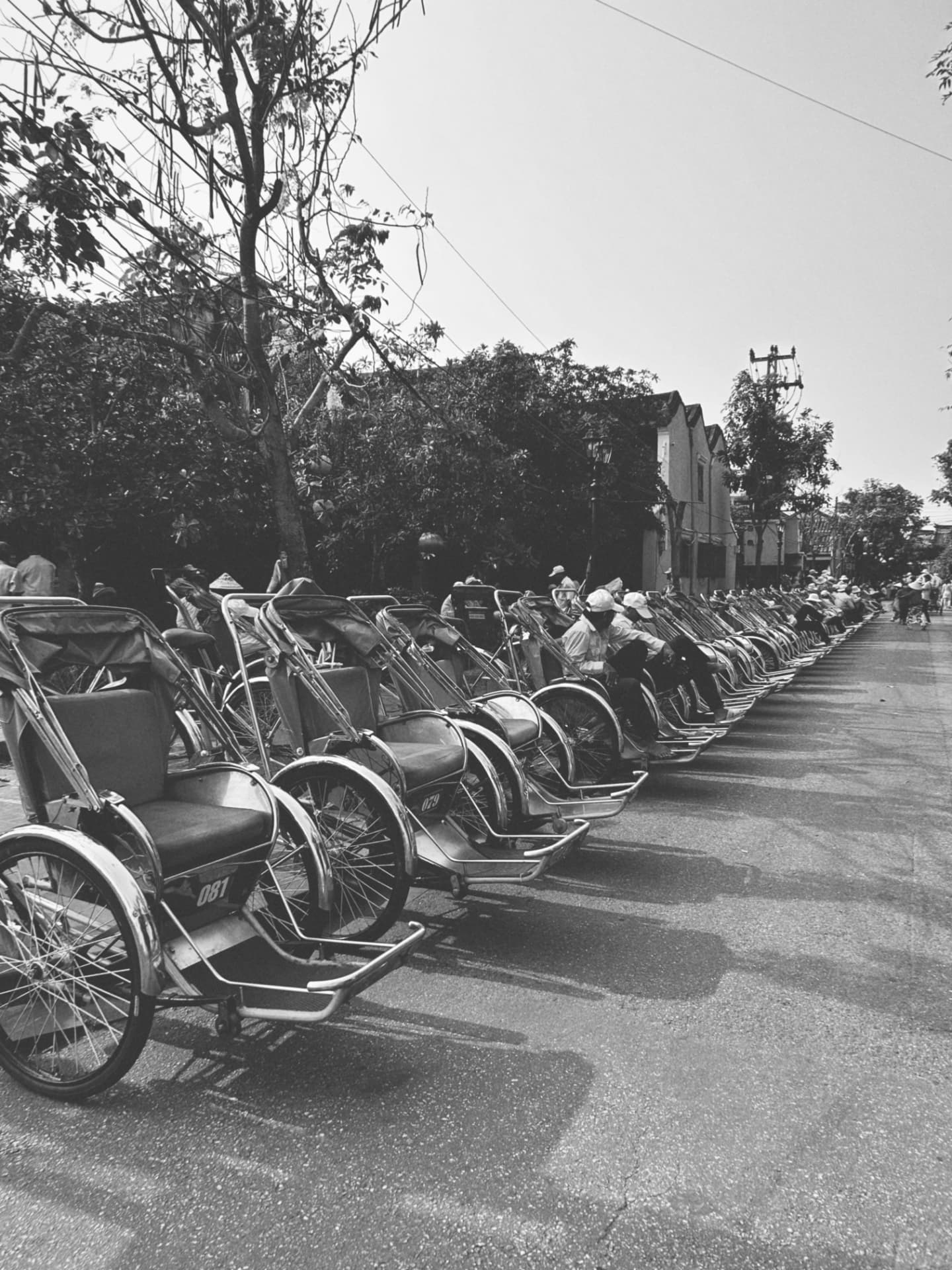 A long row of parked rickshaws and resting drivers along a street