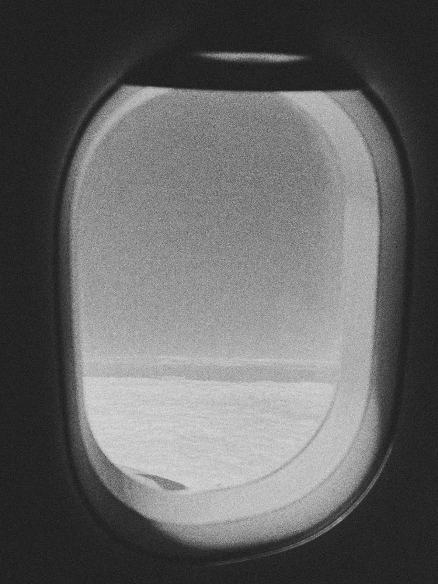 An airplane window framing open sea and a distant island