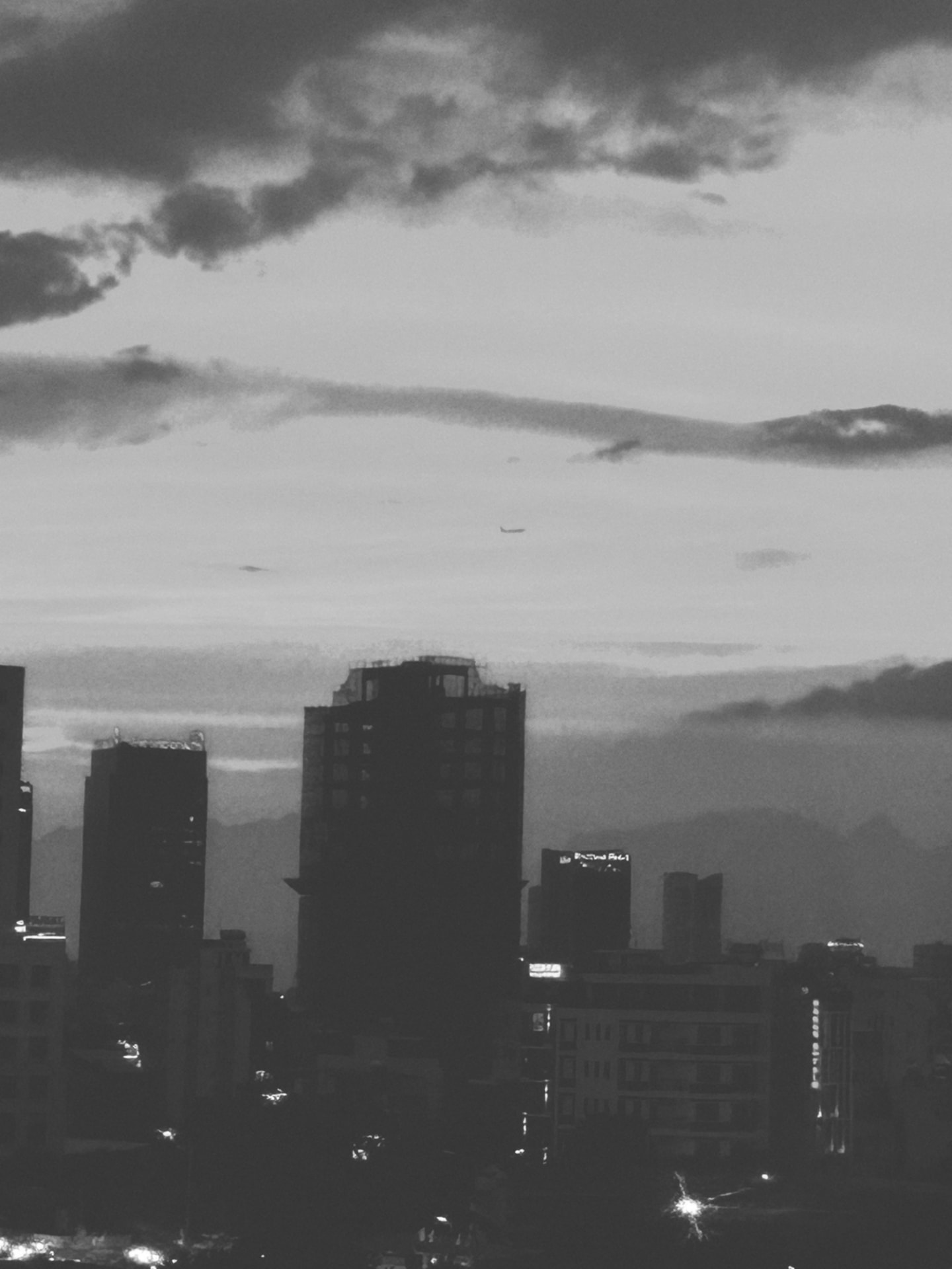 A city skyline under heavy dusk cloud with a plane crossing