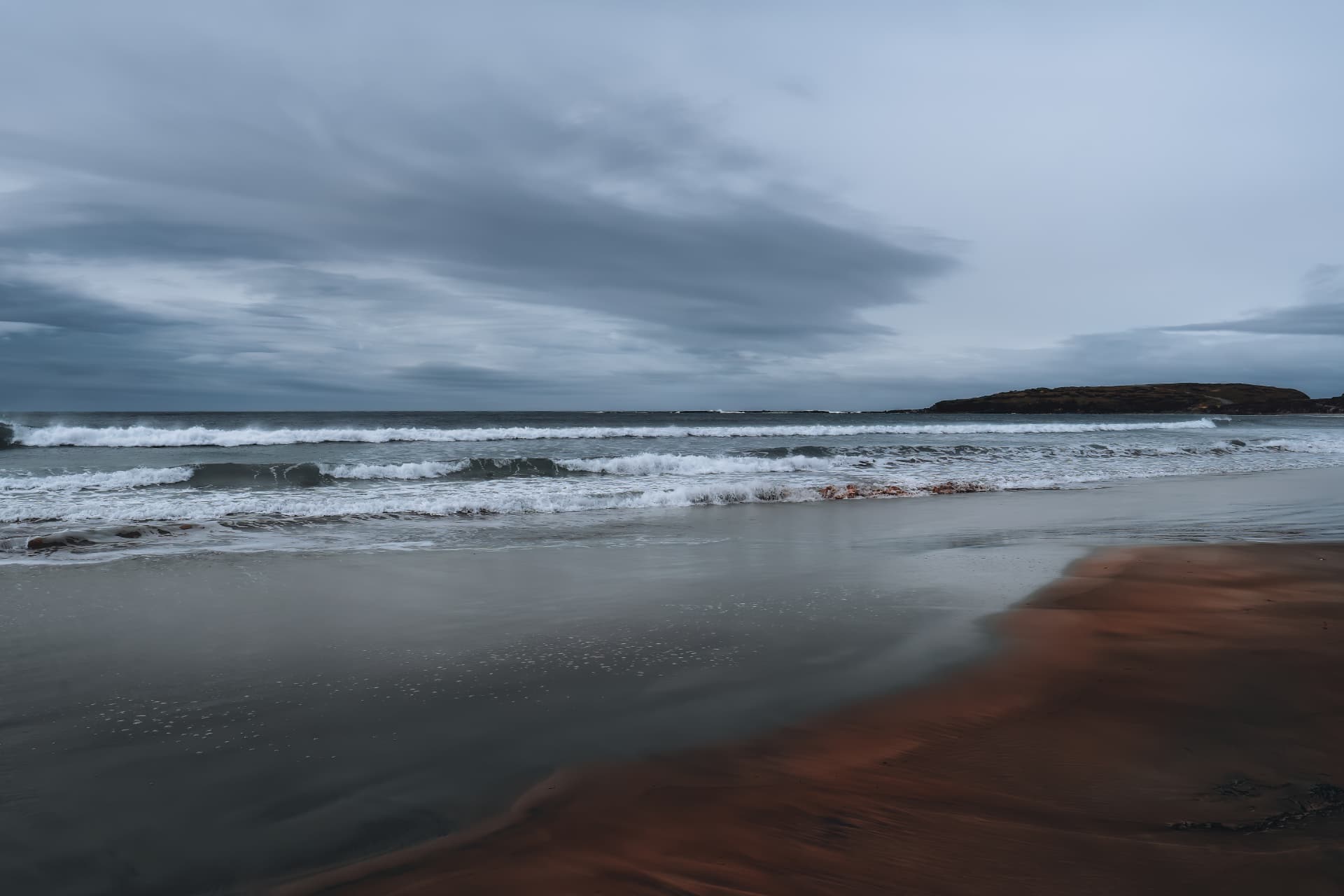 A long sandy beach with waves and a distant headland