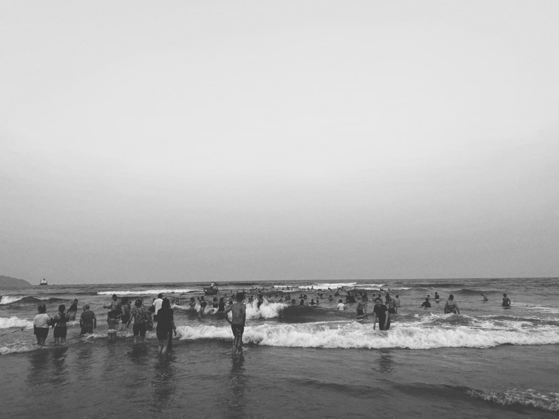 Crowds wading in low surf under a pale evening sky
