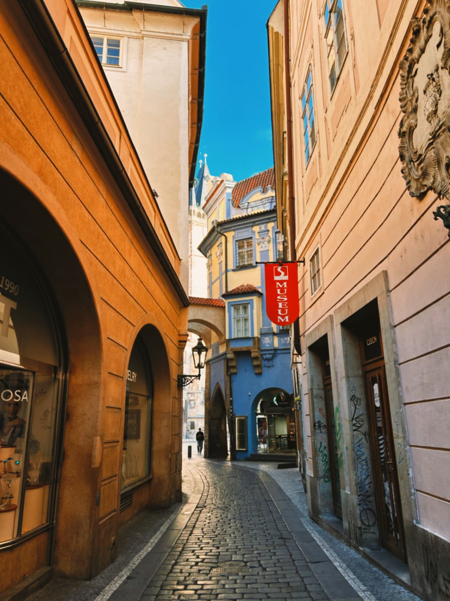 a cobbled lane with a museum sign and pastel facades