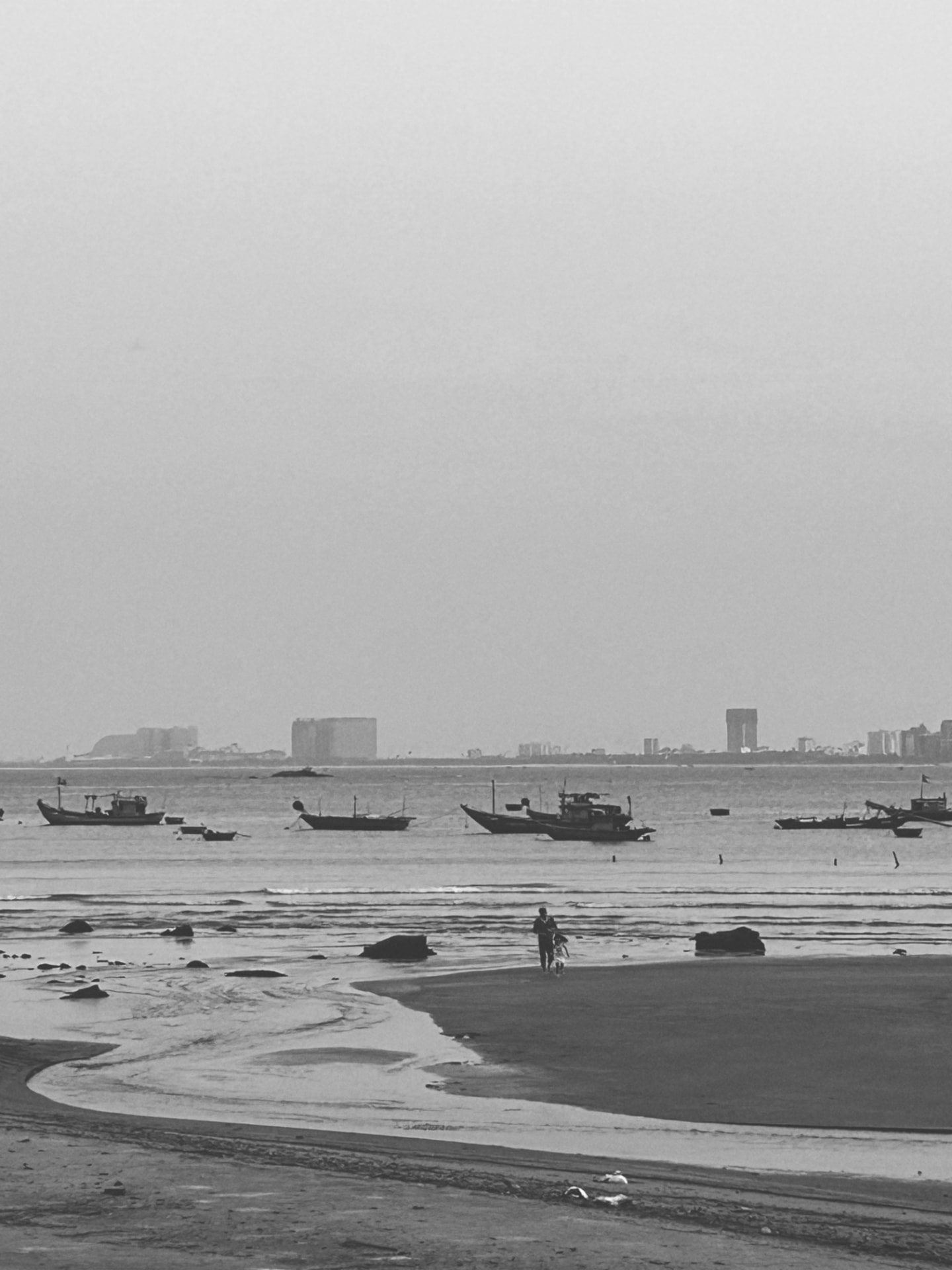 Fishing boats offshore, a figure and child walking the wet sand
