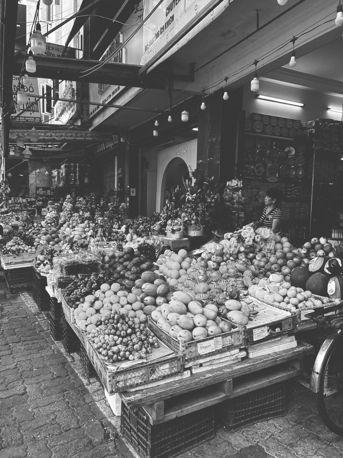 Fruit market stalls stacked under strings of hanging bulbs