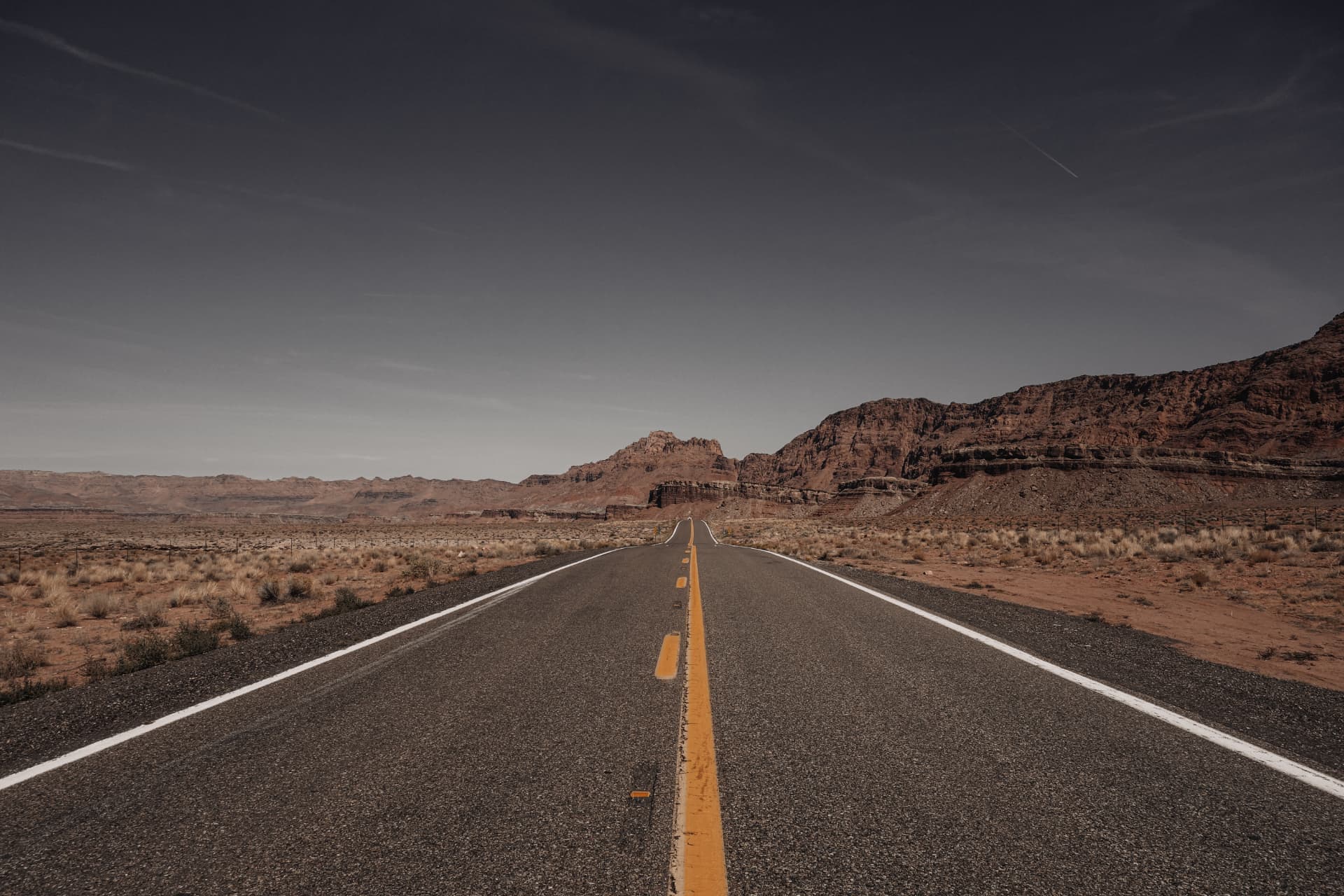An empty desert road running toward red rock mountains