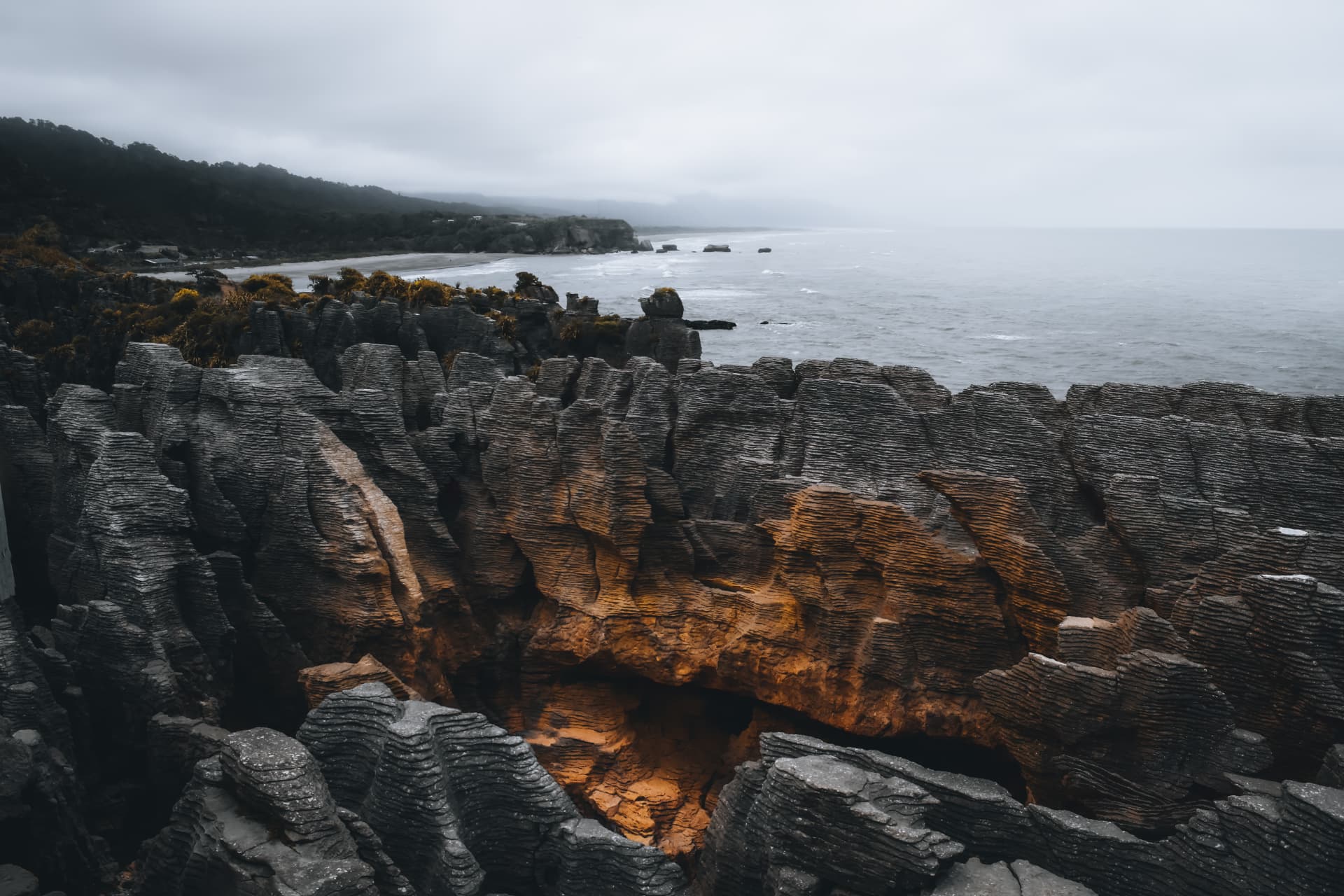 Layered coastal rock warmed by a seam of amber light above a misty shore