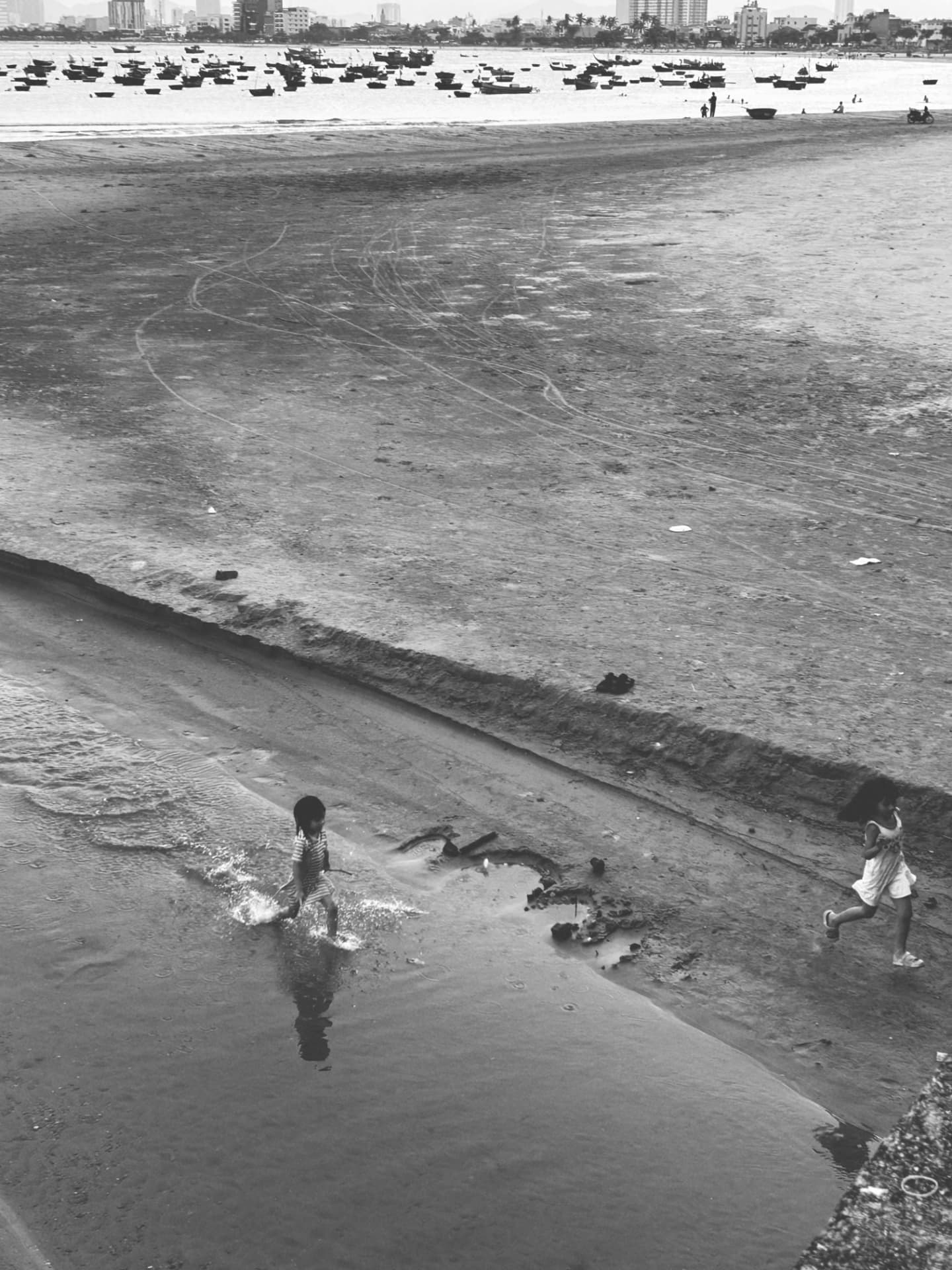Children running through tidal puddles on flat wet sand