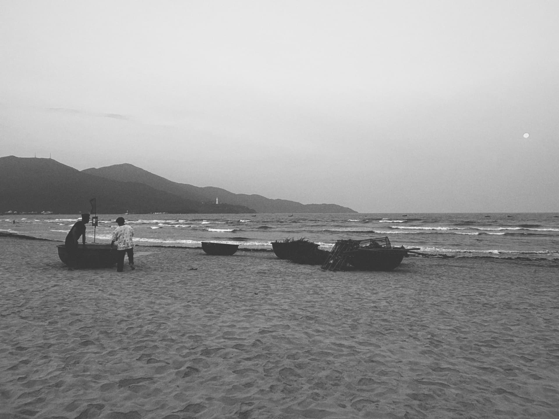Fishermen and round boats on wet sand at dusk