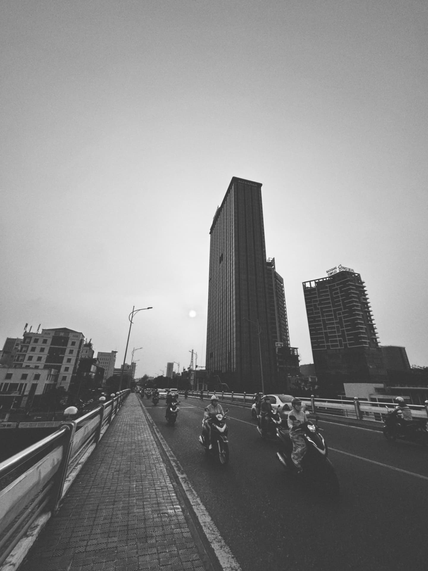 Riders crossing a bridge beneath tall towers at dusk