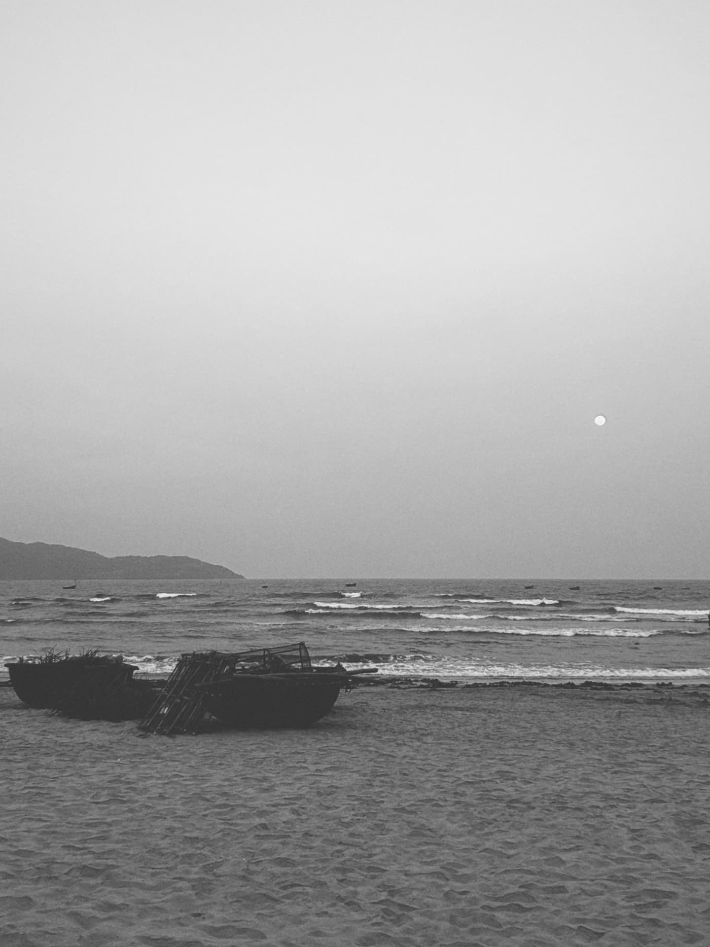 A full moon over the sea above coracle boats beached on sand