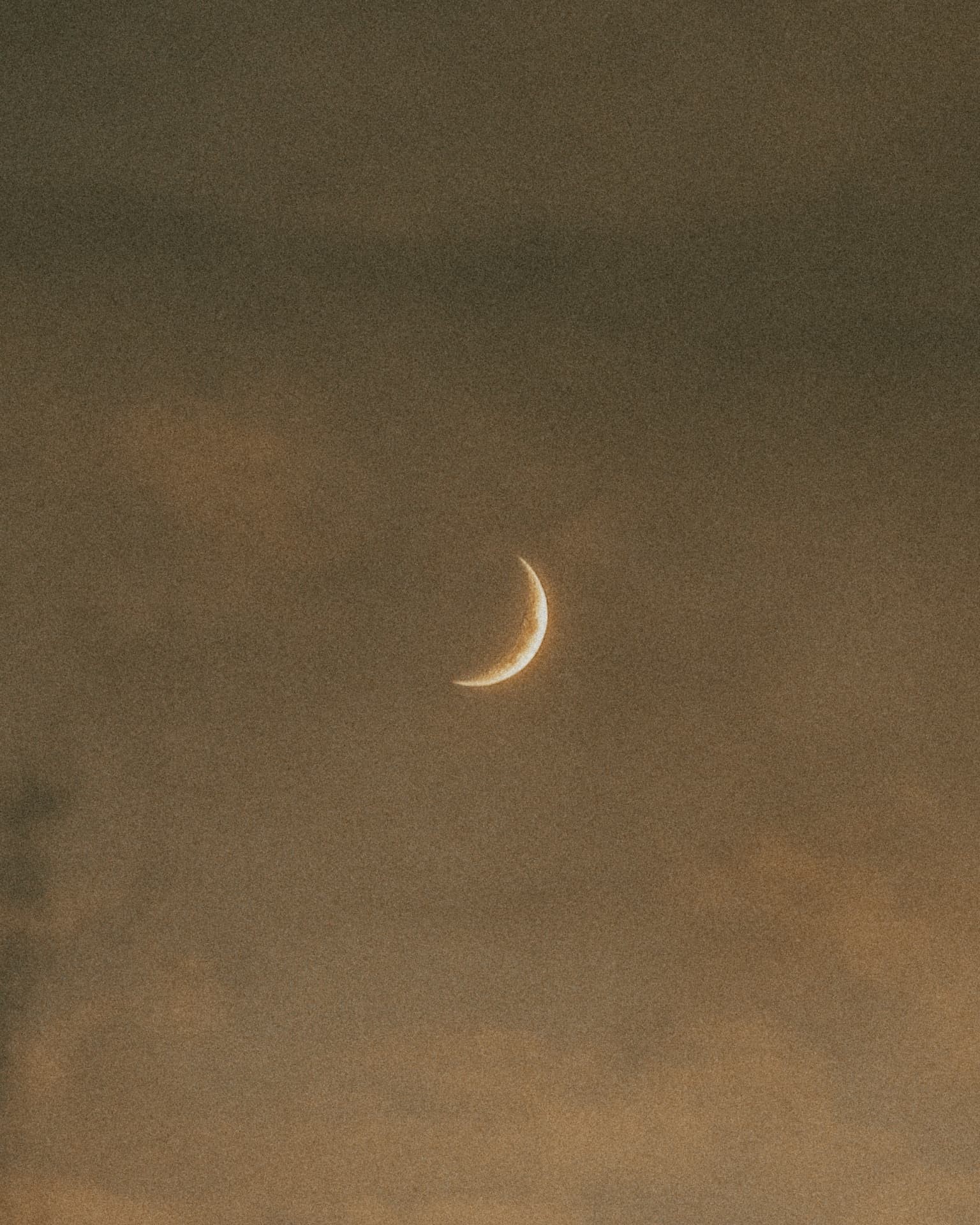 A crescent moon in a hazy dusk sky
