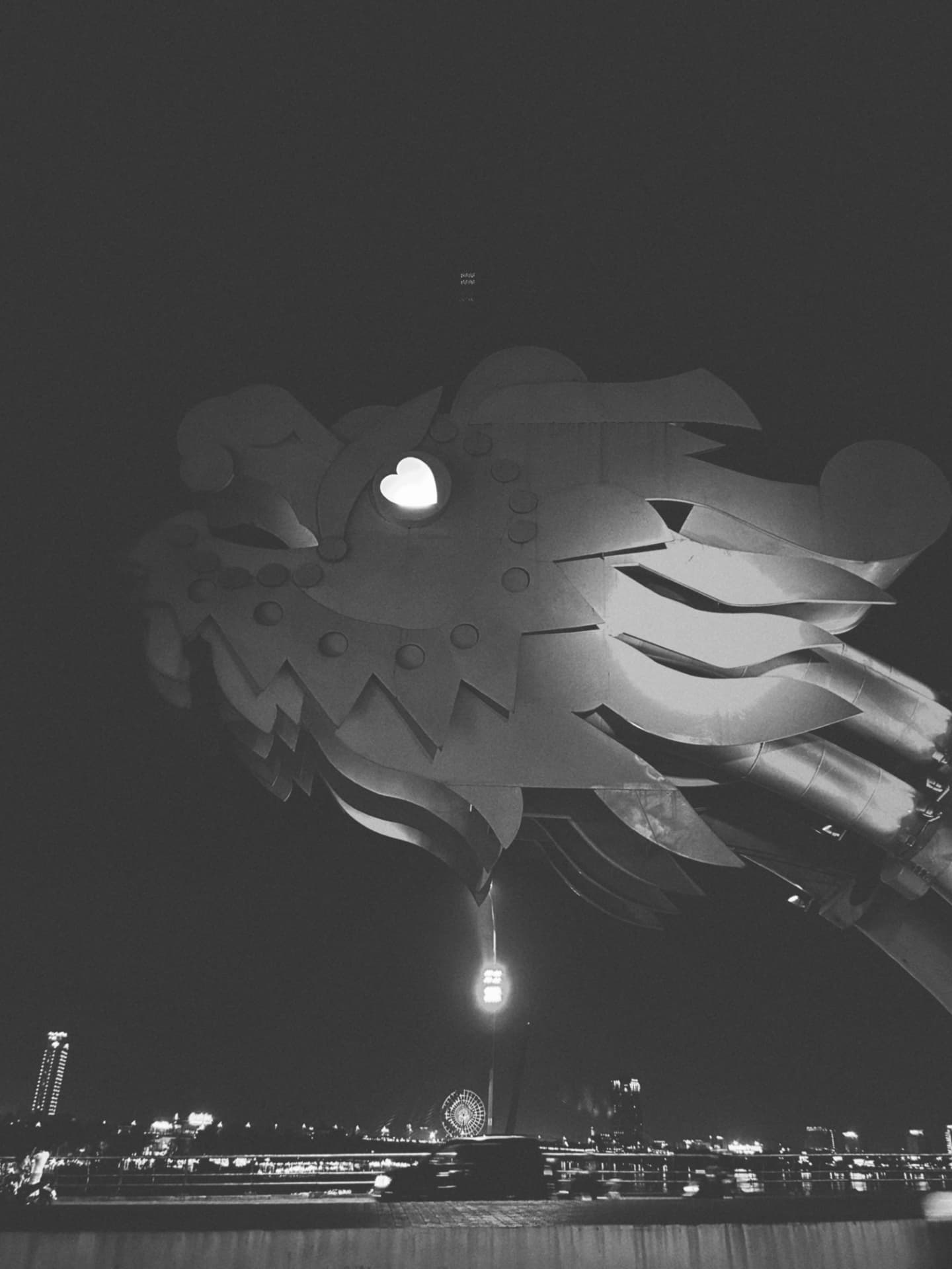 A sculpted dragon bridge head glowing above the night waterfront