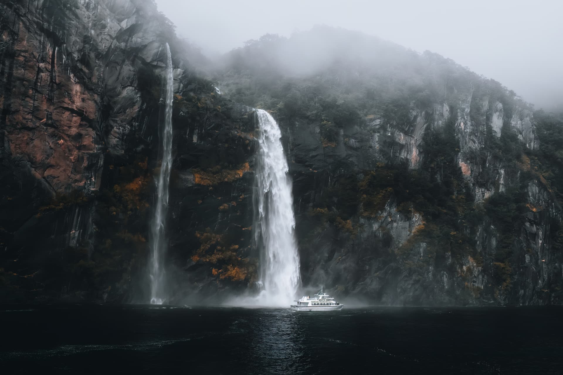 Waterfalls pouring down misty cliffs beside a small boat