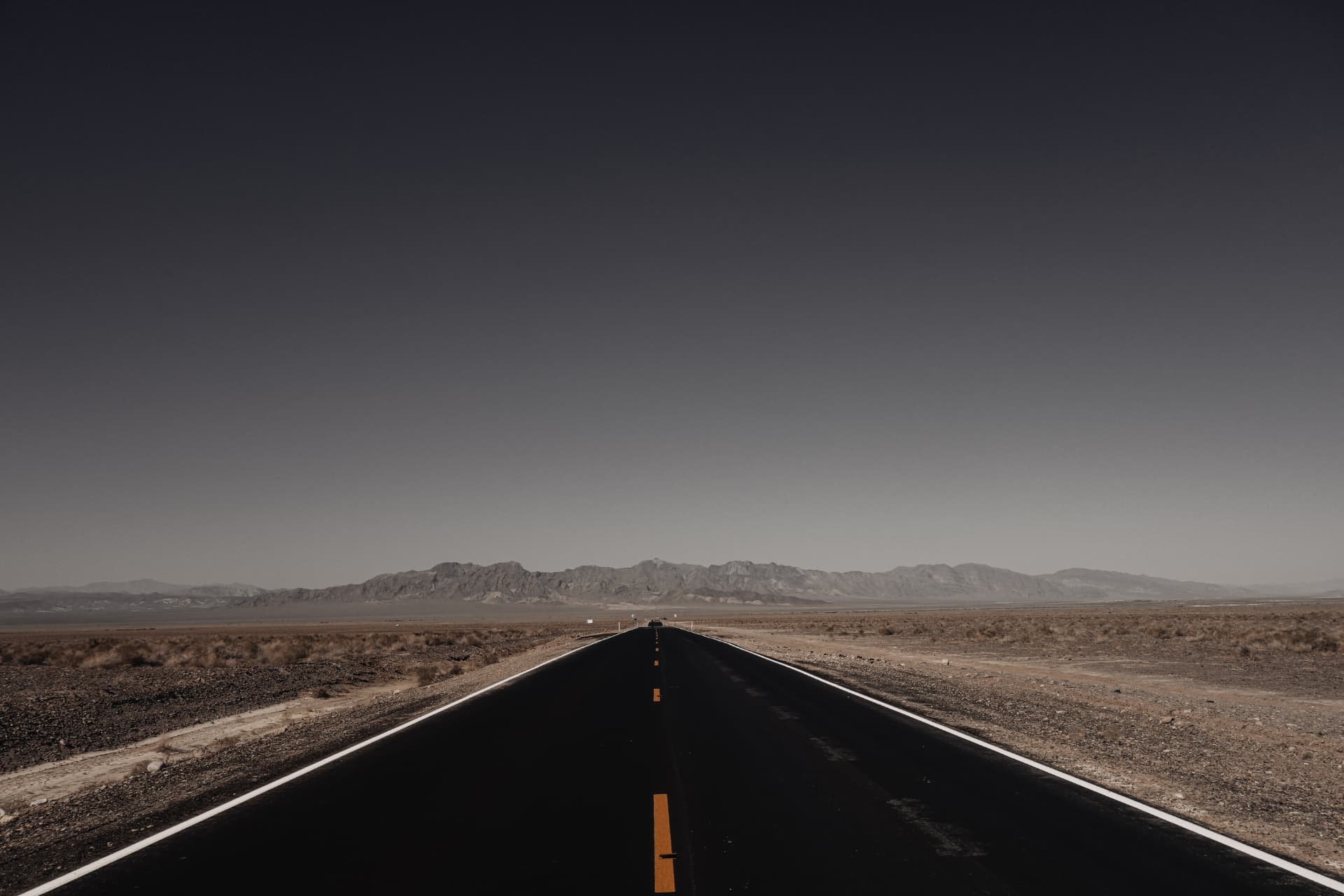 A desert road stretching to distant mountains beneath a dark sky