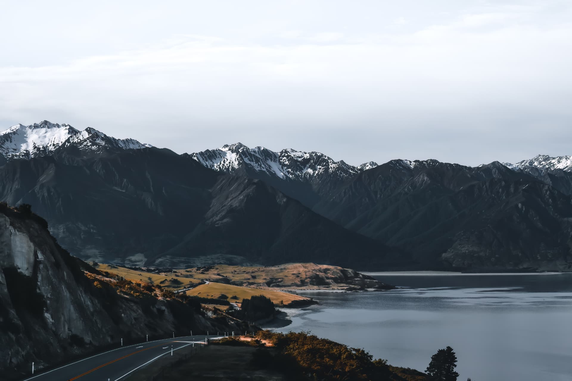 A mountain road beside a calm lake below snowy peaks