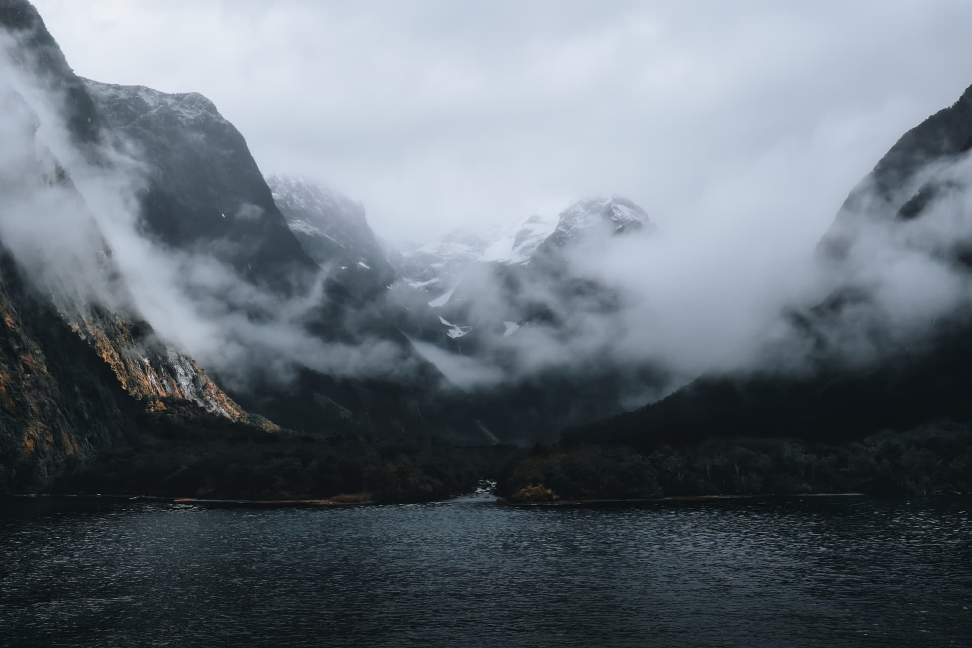 Snow-dusted peaks wrapped in cloud above a fiord
