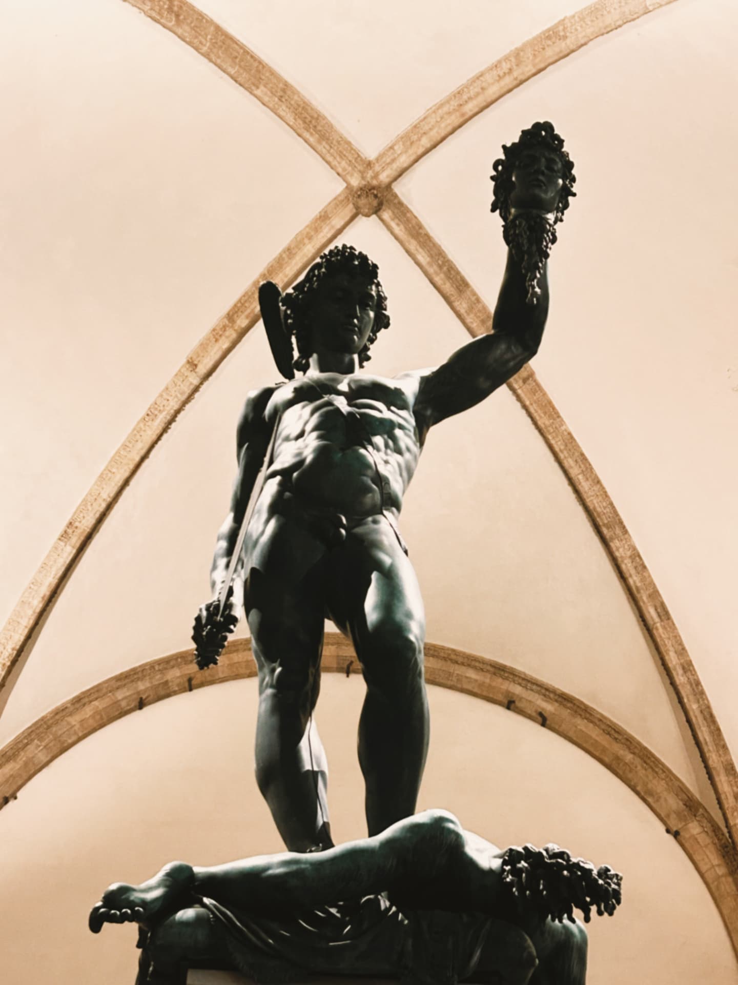 a bronze figure holding a severed head beneath arches