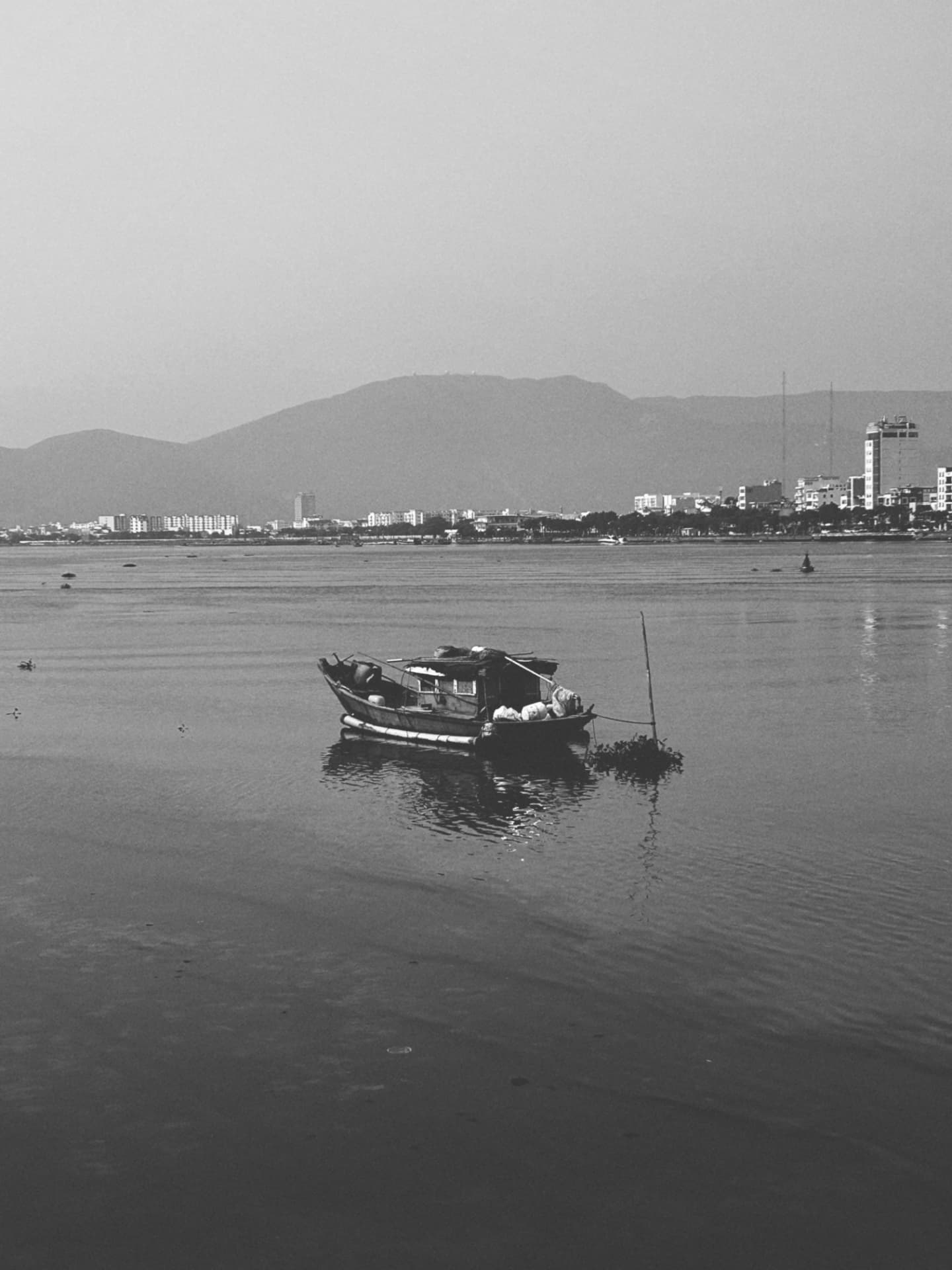 A small houseboat moored on calm water before a city shore